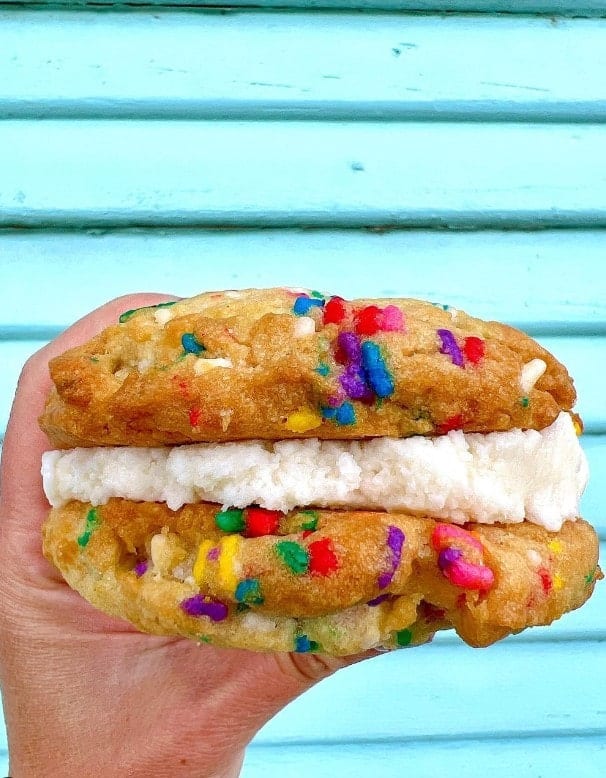 vegan sprinkle cookie sandwich with buttercream in the middle held in front of a blue wall at capital city bakery in austin