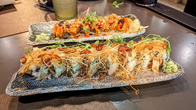 two long rectangle plates with vegan sushi rolls covered in sweet onion straws at nori in austin