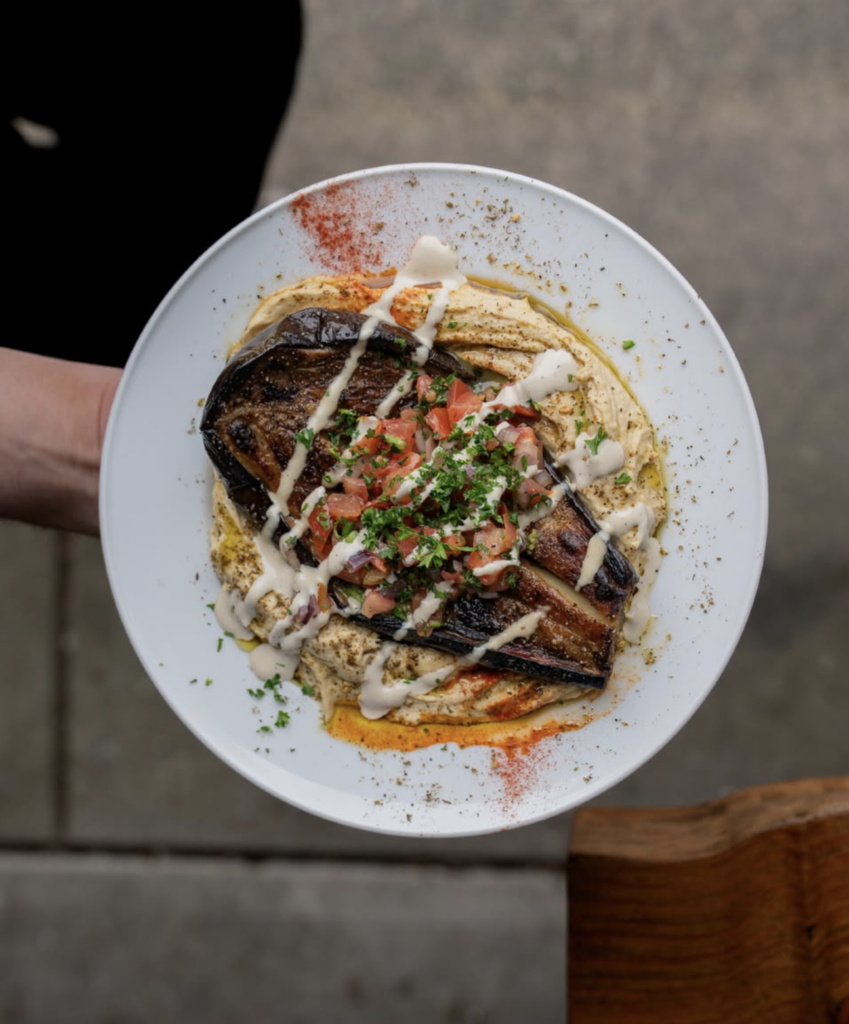 Vegan Middle Eastern dish at Chickpea Vancouver featuring roasted eggplant over creamy hummus topped with fresh herbs and tahini sauce.