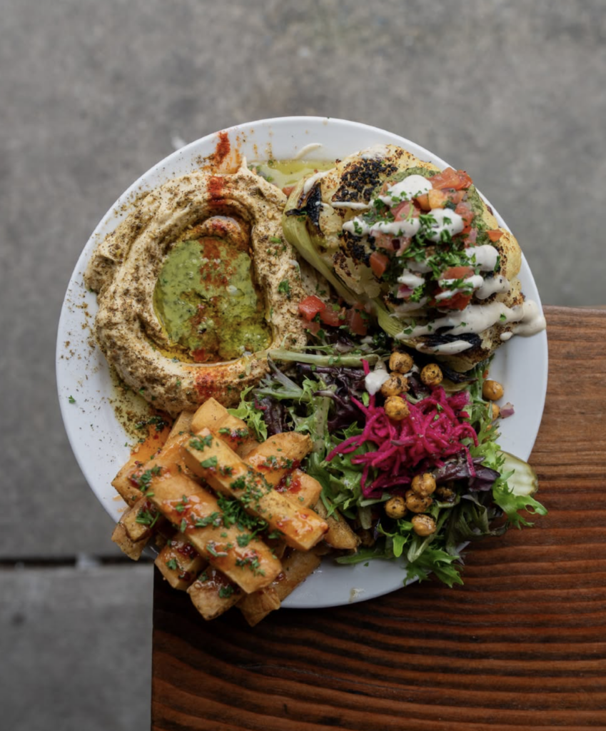 Colorful vegan platter at Chickpea Vancouver with hummus, grilled vegetables, crispy potatoes, salad, and plant-based toppings.