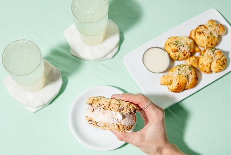 vegan ice cream sandwich held over a mint table next to a plate of garlic knots and two lemonades at virtuous pie in vancouver