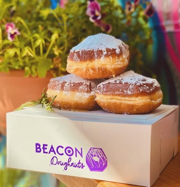 a box of vegan donuts from beacon doughnuts with three large golden glazed donuts sitting on top of the box in chicago
