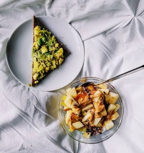 vegan oatmeal bowl with apples next to a slice of avocado toast on a white table cloth at chicago raw