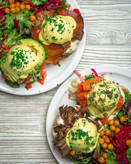 two vegan eggs benedict plates with colorful veggies and creamy yellow hollandaise on a gray table at chickpea in vancouver