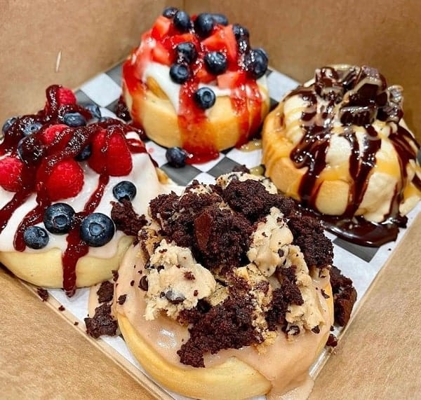 a box of four vegan cinnamon rolls topped with cookie chunks, chocolate drizzle, blueberries, raspberries, and more from cinnaholic in chicago
