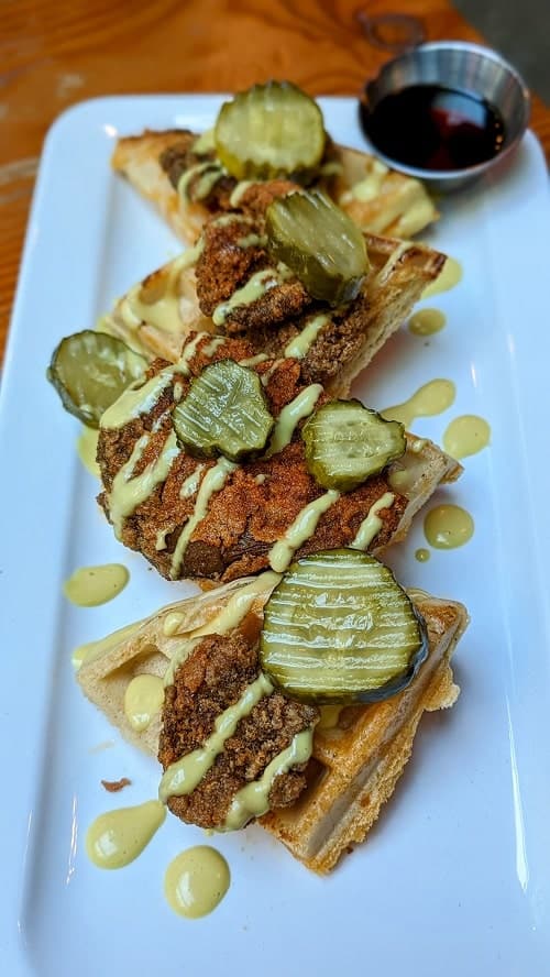 a plate of golden waffles topped with vegan fried chicken, yellow mustard sauce, and pickles at meet in vancouver