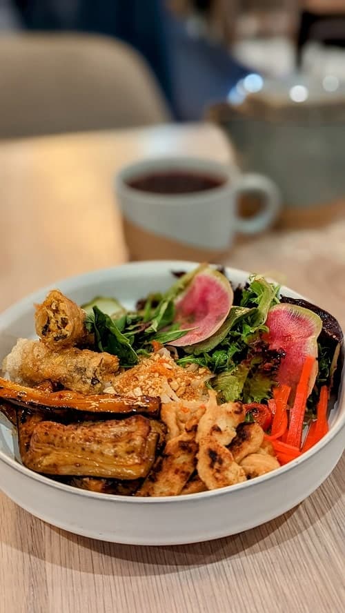 a bowl of vegan spicy noodles with tofu and veggies on a light wood table at nightshade in vancouver