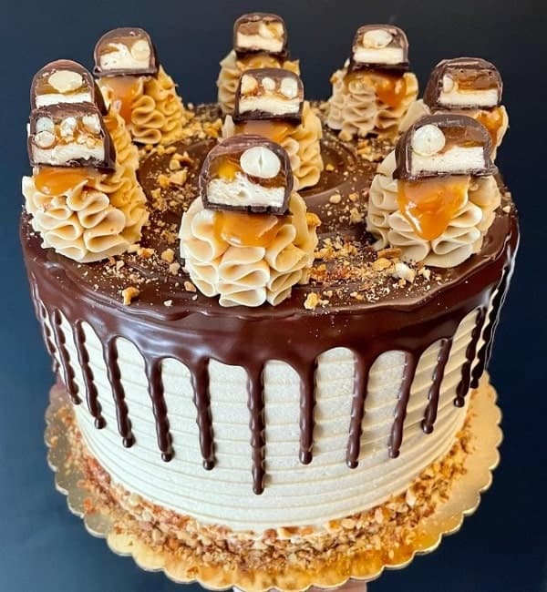 round vegan chocolate cake topped with chocolate that is drizzled down the sides and mounds of buttercream topped with candy chunks in chicago