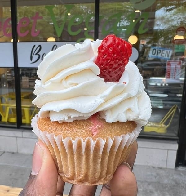 a single vegan vanilla cupcake topped with vanilla butter cream and a strawberry slice held in front of sweet vegan bakes in chicago