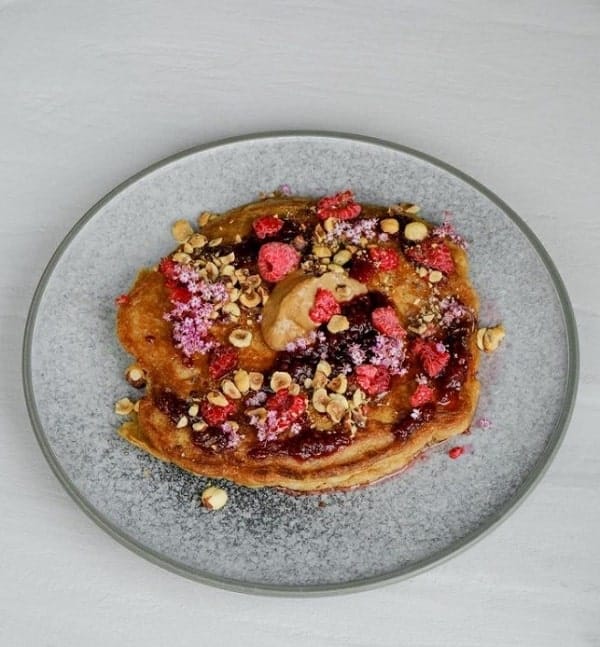 vegan pancakes topped with fresh berries and granola on a gray plate at the acorn in vancouver