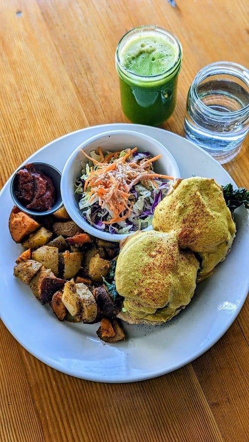 vegan tofu benny plate with potatoes sitting next to a green juice and water at eternal abundance in vancouver