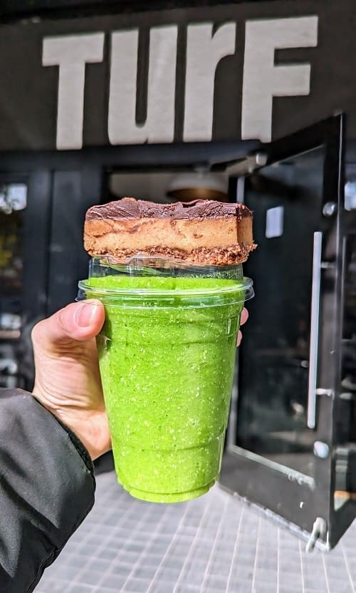 vegan green smoothie with a raw vegan chocolate bar sitting on top held in front of the turf restaurant sign in vancouver