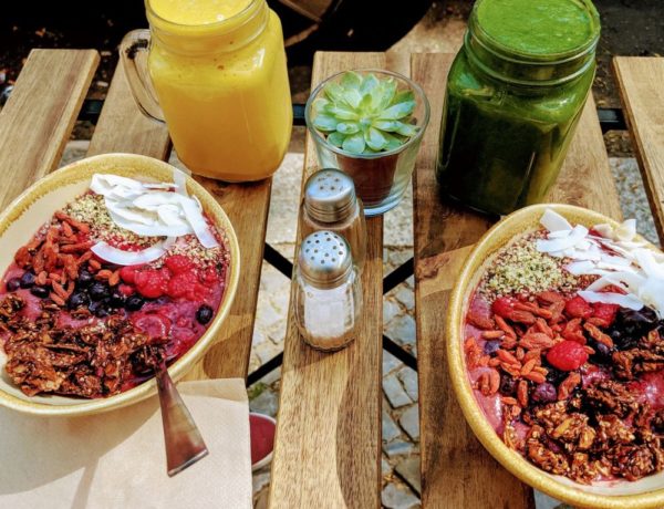 two vegan acai bowls sitting on a wooden table next to a yellow and green smoothie in the summer in berlin