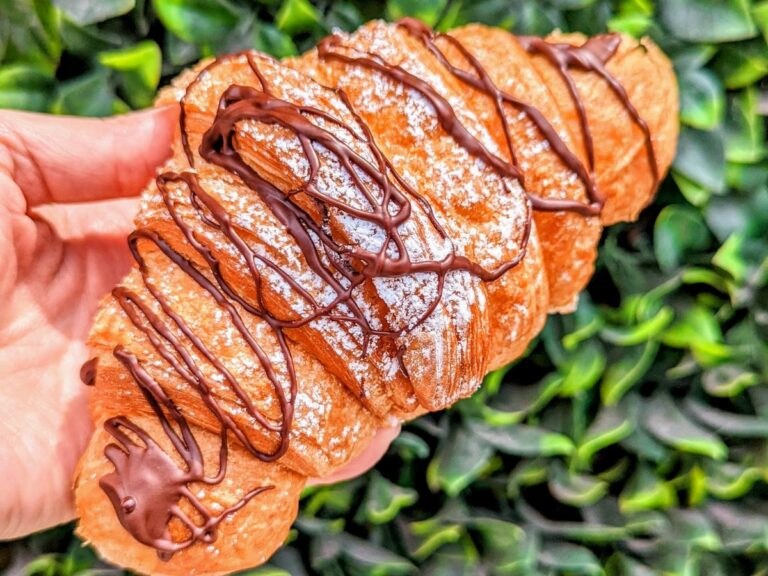 vegan chocolate croissant in front of a green bush from the vegan danish bakery on queens in toronto