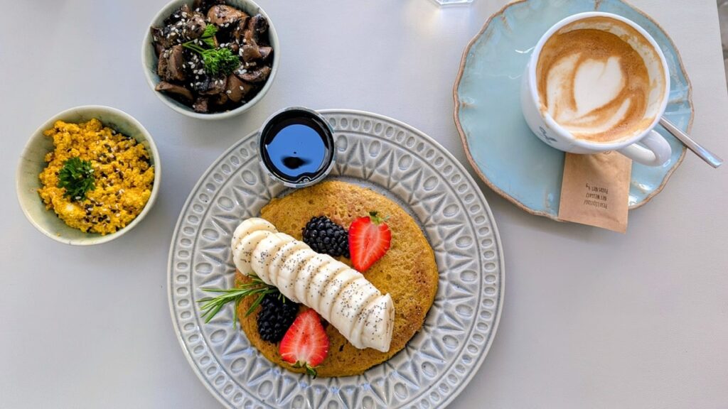 a plate with a vegan pumpkin pancake topped with banana slices next to a tofu scramble with roasted mushrooms at Manjerica in lisbon