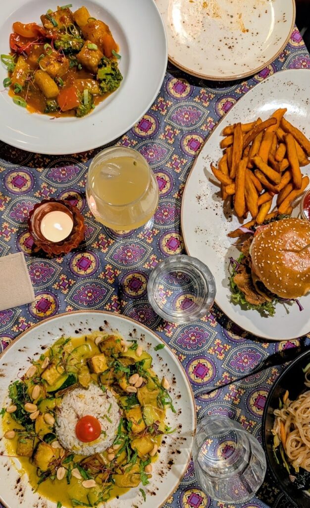 three vegan dishes on a purple tableclothed table with drinks and empty dishes at psi restaurant in lisbon