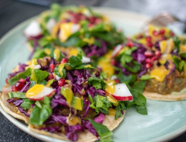 a plate of three vegan tacos topped with colorful slaw and sauce