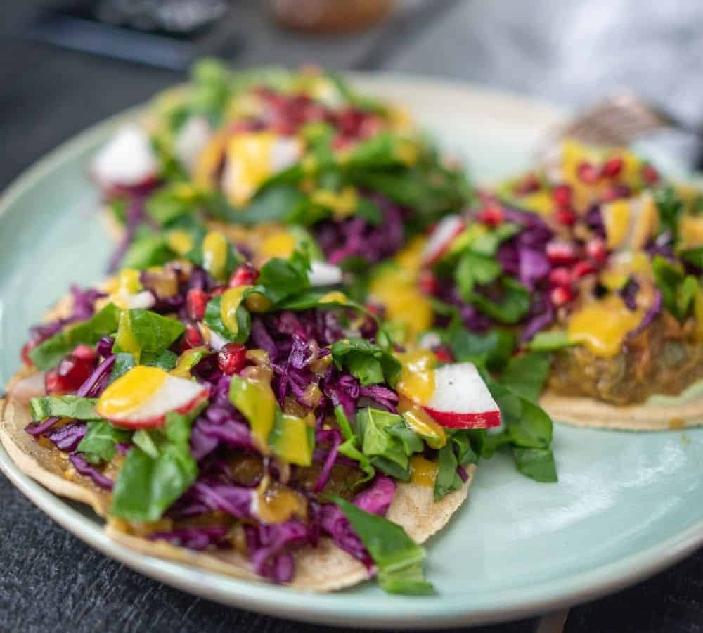 a plate of three vegan tacos topped with colorful slaw and sauce