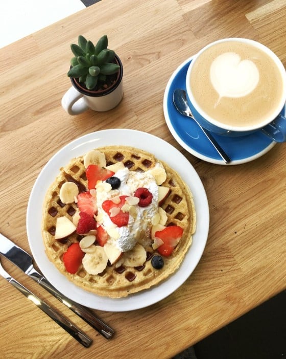 a vegan belgian waffle topped with fresh blueberries and strawberries next to a latte with a white heart in paris