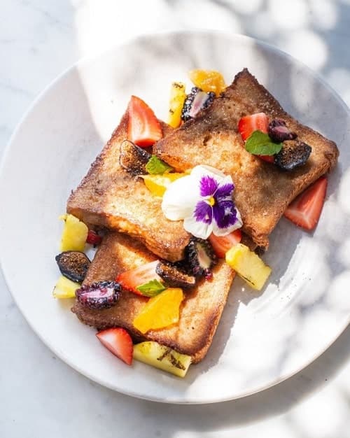 a stack of golden vegan french toast covered in fruit on a white plate at gracias madre in la