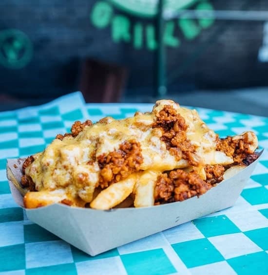 a brown paper tray filled with vegan french fried covered in chili and cheese sauce from grilled in brooklyn