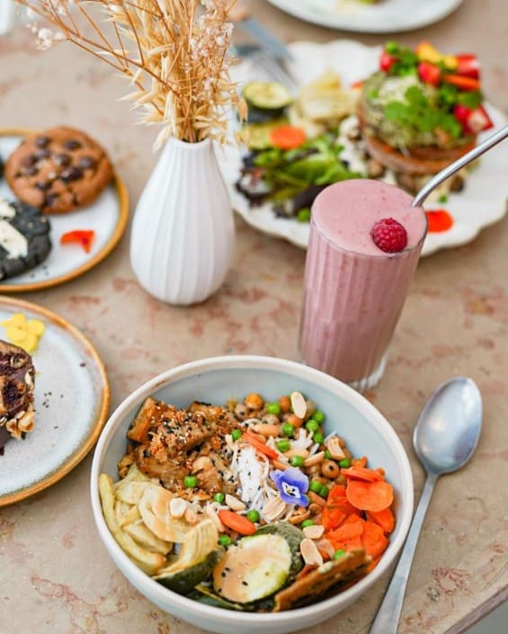 a colorful display of vegan brunch and lunch dishes with a pink strawberry milkshake on a light wood table in paris