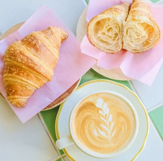 two vegan croissants next to an oatmilk latte sitting on pink napkins at kitchen mouse in LA