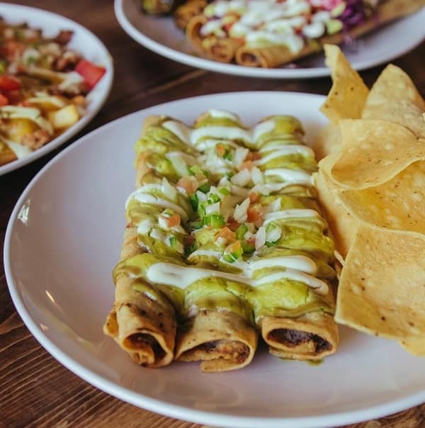 a plate of three vegan flautas covered in avocado sauce next to tortilla chips at lick it up austin
