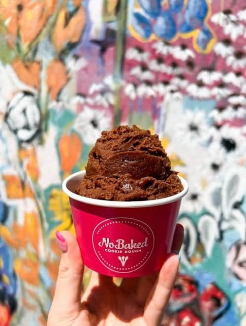 a scoop of vegan chocolate cookie dough in a pink cup in front of a nashville mural