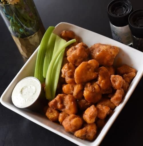 a square dish filled with vegan buffalo cauliflower wings next to a dipping sauce and celery at the vegan bar north star lounge in ann arbor