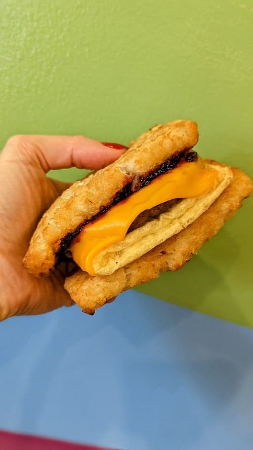 vegan breakfast sandwich with a hashbrown bun held in front of a green and blue wall at sookies veggie burgers in madison