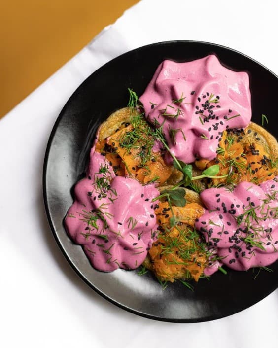 a black round bowl filled with an alternating mix of purple beet cream sauce and an orange veggie in paris