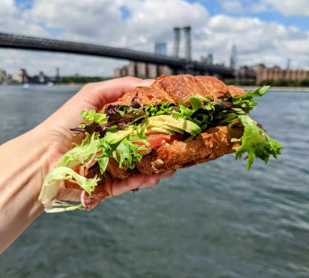 vegan croissant sandwich with the brooklyn bridge in the background