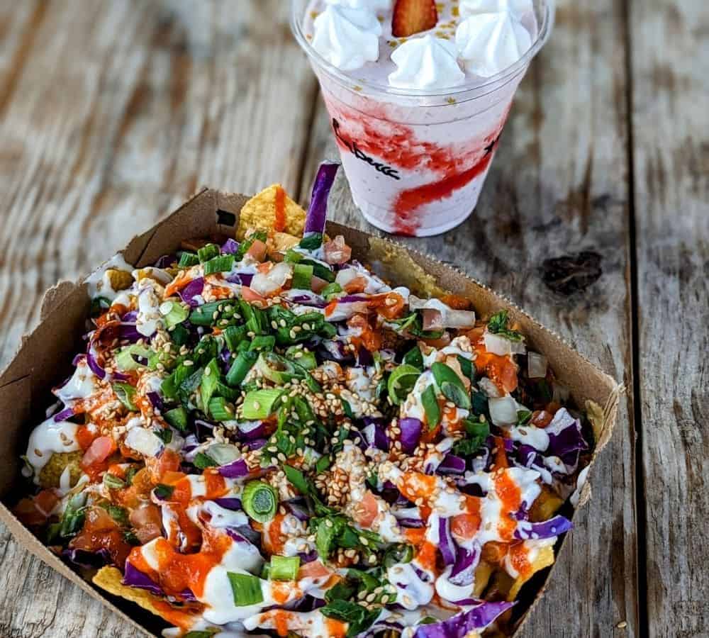 a paper tray with vegan nachos covered in cheese and hot sauce next to a strawberry milkshake in austin