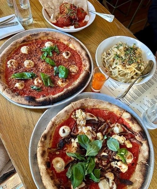 two vegan pizzas side by side next to a bowl of creamy pasta on a dining table at double zero in nyc