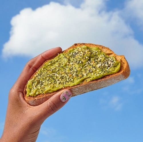 a slice of avocado toast held up in the sky with one cloud behind it from dunkin donuts