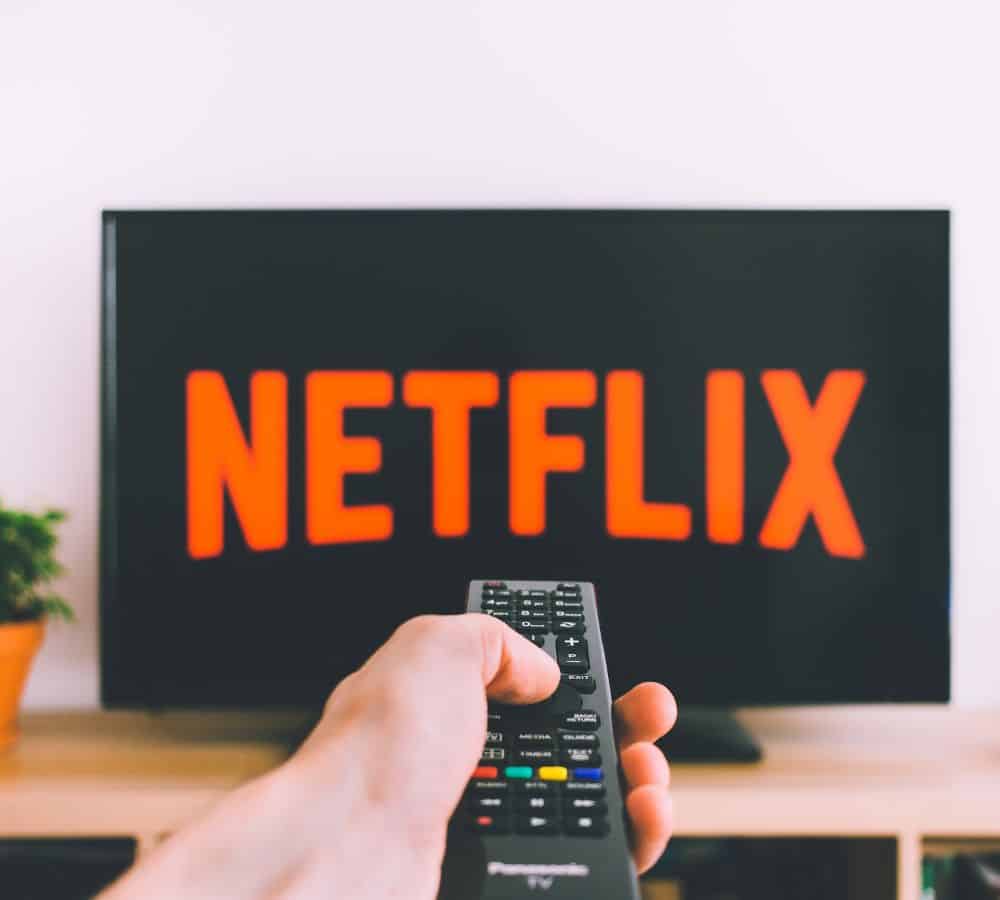 tv screen with netflix logo and a person hold a remote control in front of it