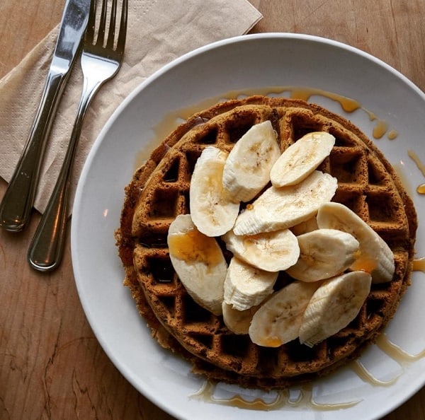 giant vegan Belgian waffle topped with banana slices and syrup on a white plate at nourish café in San Francisco