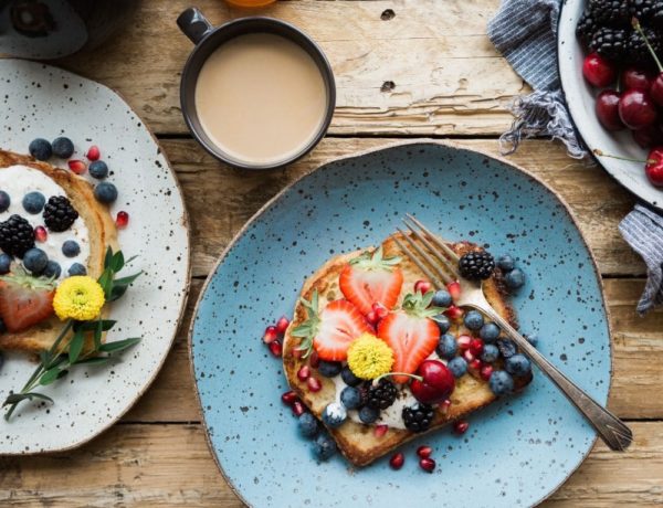 breakfast toast covered in fresh fruit next to a coffee mug on a wood table
