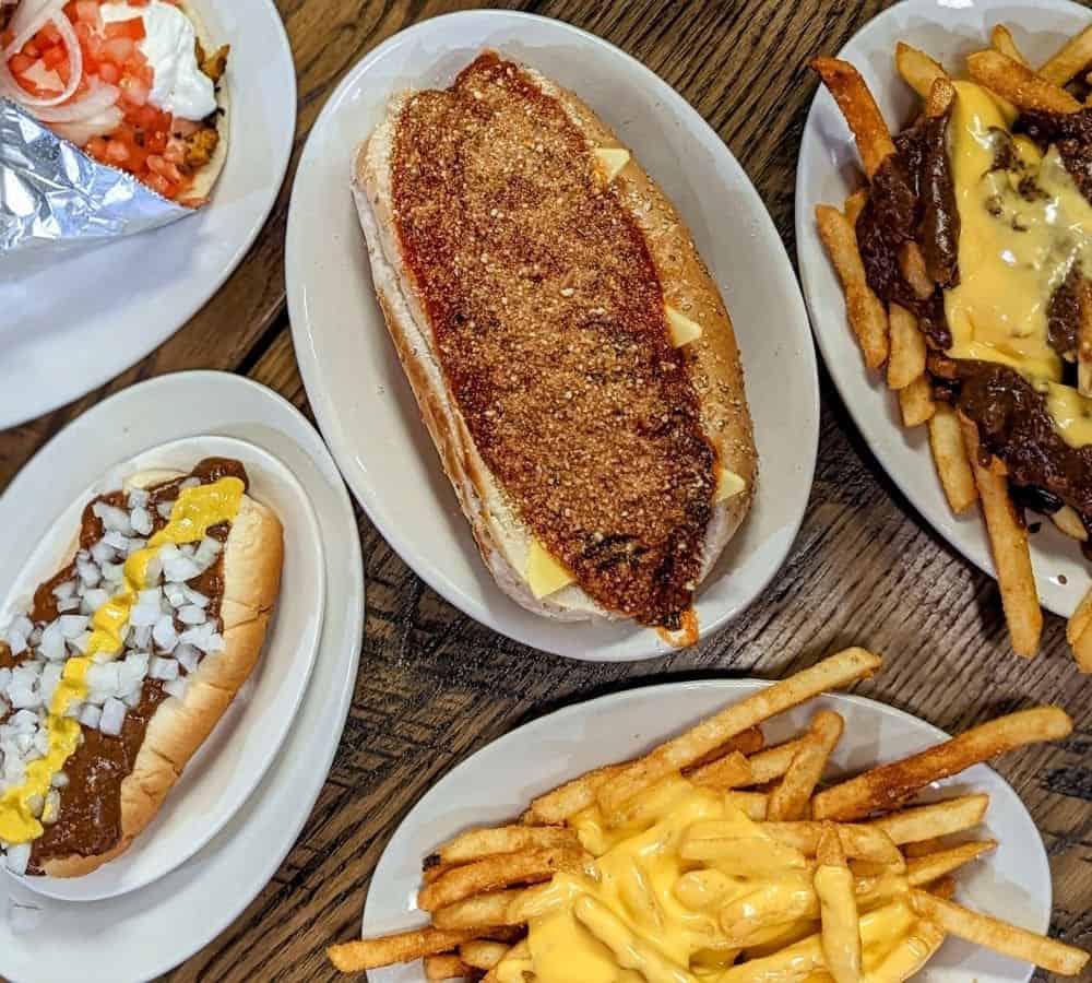 spread of vegan fast food options like cheese covered fries, chili cheese dog, chicken parm sandwich
