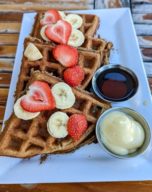 a stack of golden vegan and gluten free waffles topped with strawberries and banana slices at delicious raw in miami