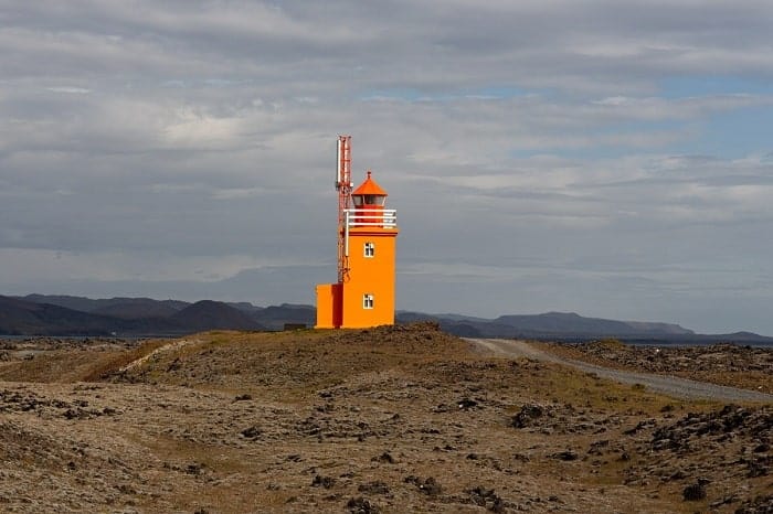 a bright orange light house in the middle of iceland's desolate landscape on a cloudy day