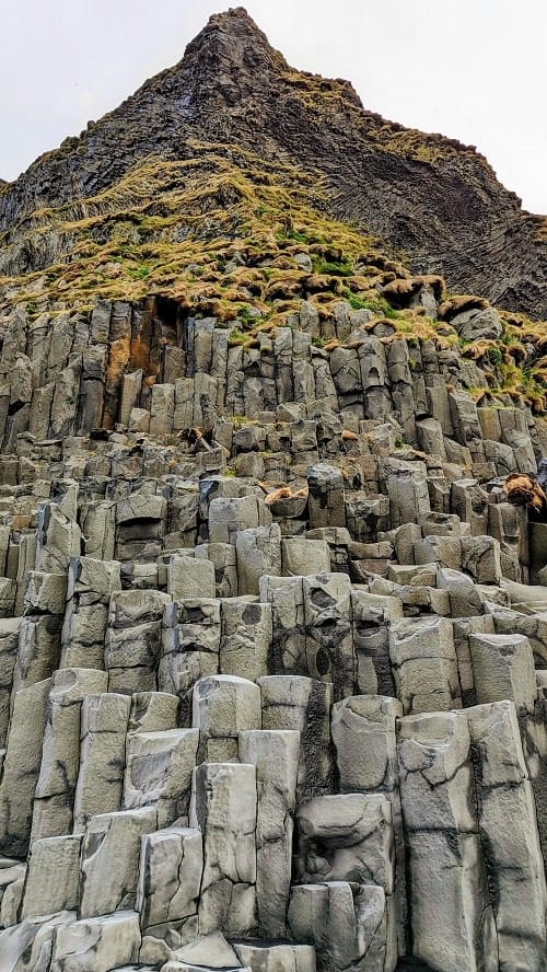 basalt column on a tall cliff at the dangerous Reynisfjara Beach on a cloudy and windy day in iceland on a day trip from Reykjavik