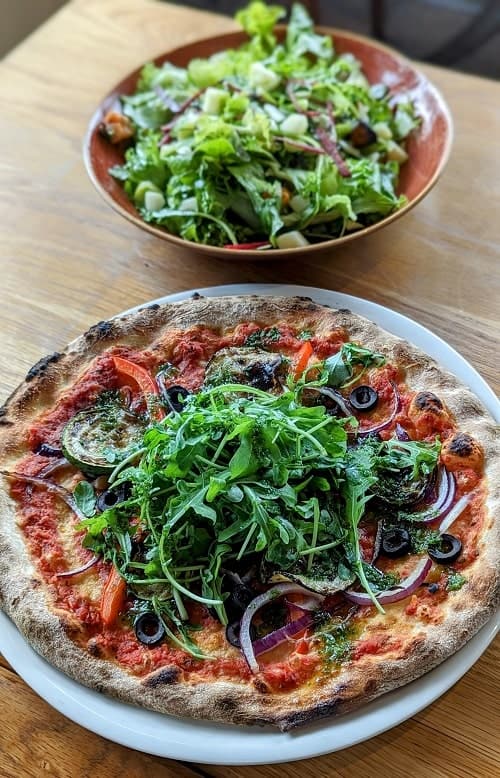 a vegan pizza topped with arugula in front of a salad at the bautinn restaurant in akureyri iceland