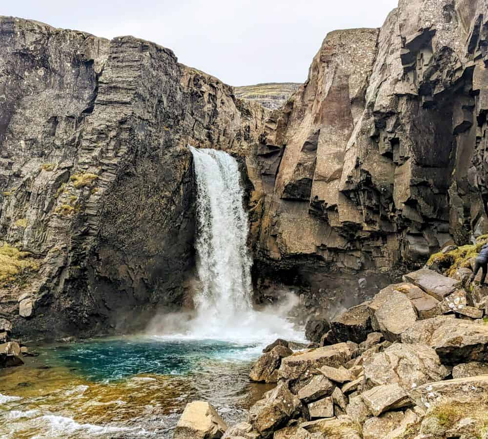 hidden waterfall flowing into a blue pool off of the side of the road in iceland
