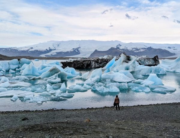 the jokulsarlon glacier lagoon filled with icebergs and a person standing at the waters edge in iceland