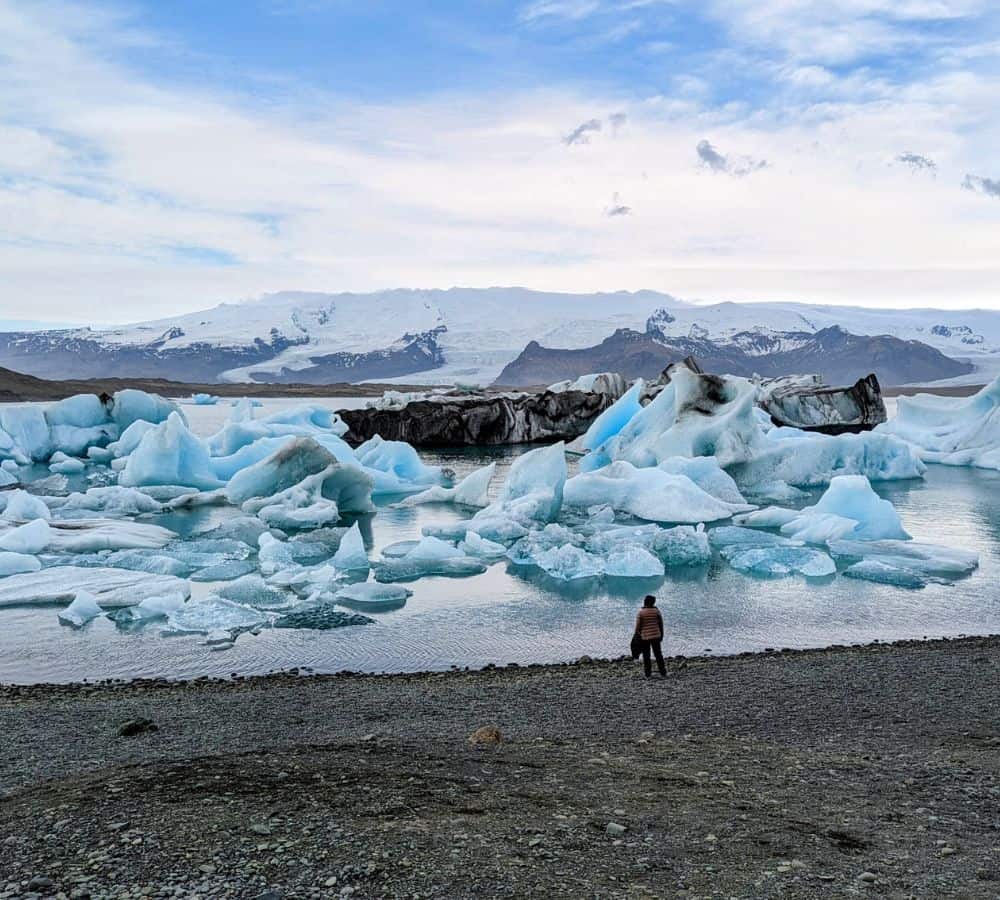 the jokulsarlon glacier lagoon filled with icebergs and a person standing at the waters edge in iceland
