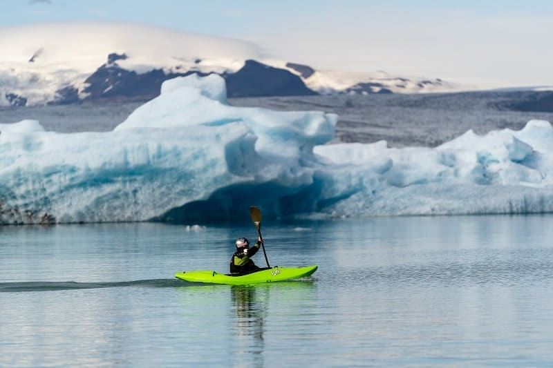 a bright green kayak in the middle of a glacial lagoon with icebergs in iceland