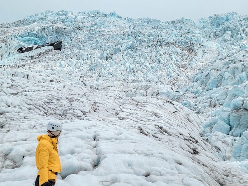hiking the white and icy blue vatnajokull glacier in iceland with a person in a yellow jacket standing at the base