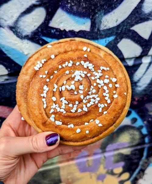 golden vegan cinnamon roll topped with sugar in front of a colorful mural at braud in Reykjavik